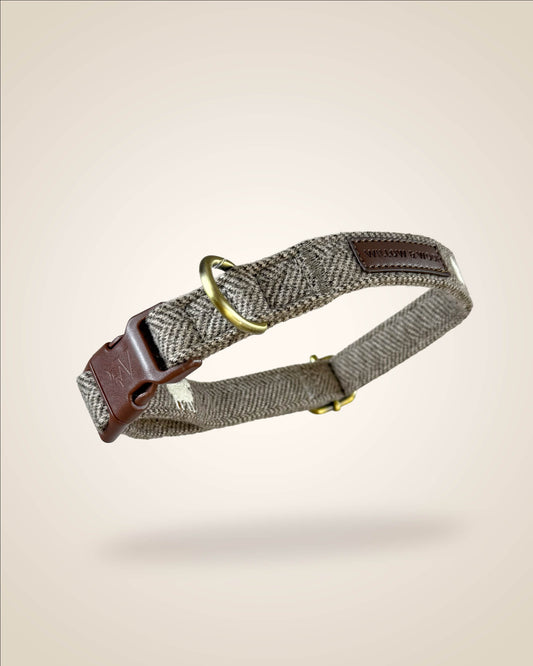 A brown and white tweed herringbone patterned dog collar with white sheep motifs, bronze tone hardware, and a brown leather patch, shown against a light beige background.