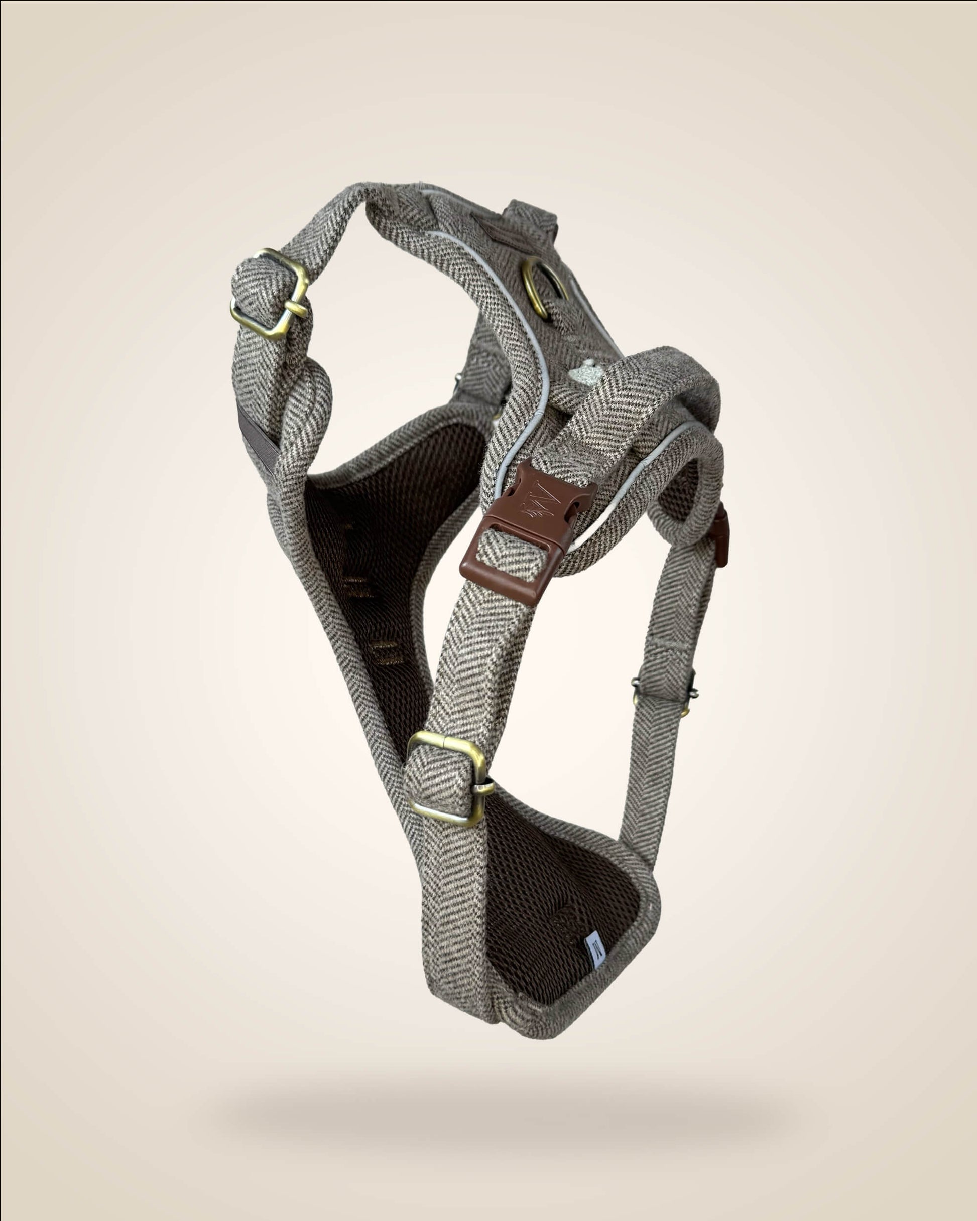 A brown and white tweed herringbone patterned dog harness with white sheep motifs, bronze tone hardware, and a brown leather patch, shown against a light beige background.